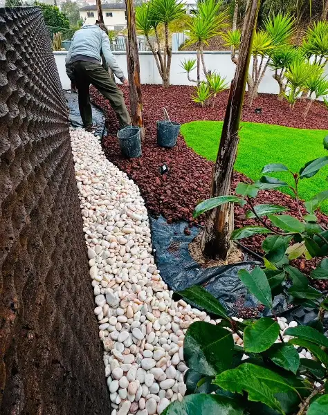 Jardim de moradia com palmeiras, seixo branco e relva sintética — durante a obra