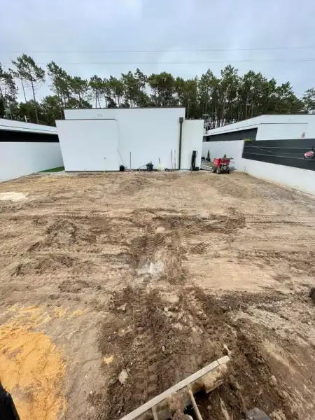 Jardim amplo com relva sintética, caminhos em lajes e zona de fogueira — antes da obra