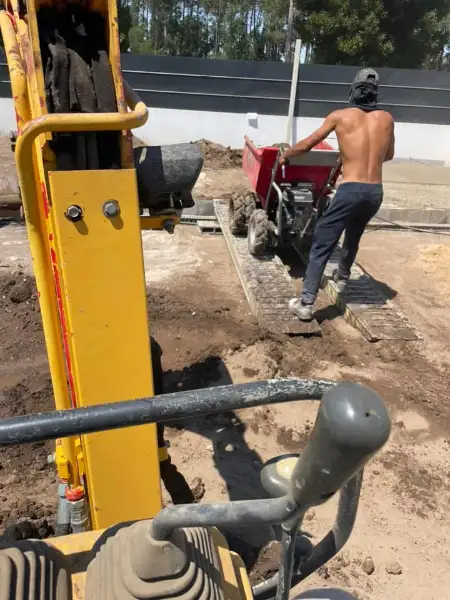 Jardim amplo com relva sintética, caminhos em lajes e zona de fogueira — durante a obra