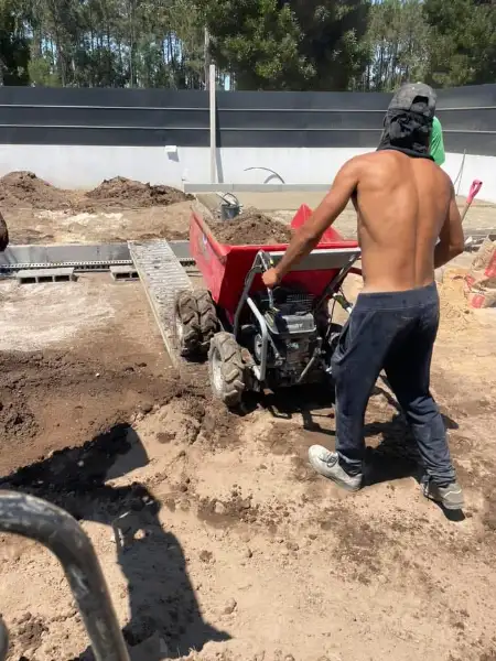Jardim amplo com relva sintética, caminhos em lajes e zona de fogueira — durante a obra