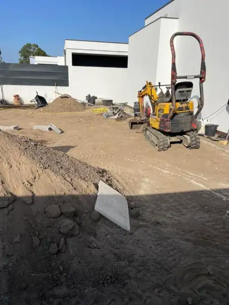 Jardim amplo com relva sintética, caminhos em lajes e zona de fogueira — durante a obra
