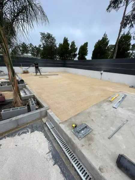 Jardim amplo com relva sintética, caminhos em lajes e zona de fogueira — durante a obra