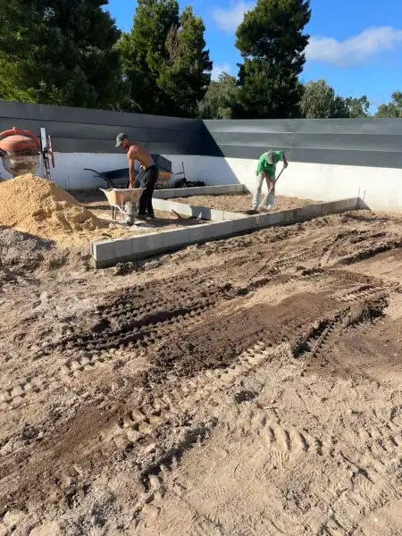 Jardim amplo com relva sintética, caminhos em lajes e zona de fogueira — durante a obra