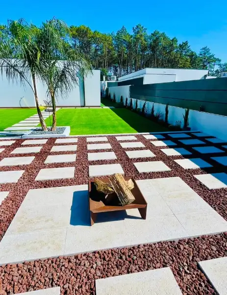 Jardim amplo com relva sintética, caminhos em lajes e zona de fogueira — resultado final