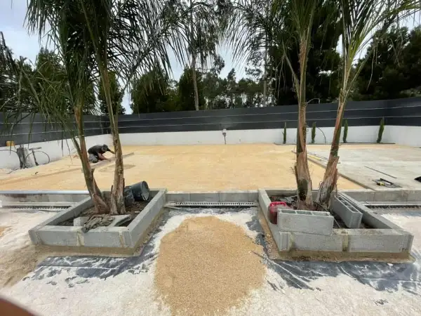 Jardim amplo com relva sintética, caminhos em lajes e zona de fogueira — durante a obra