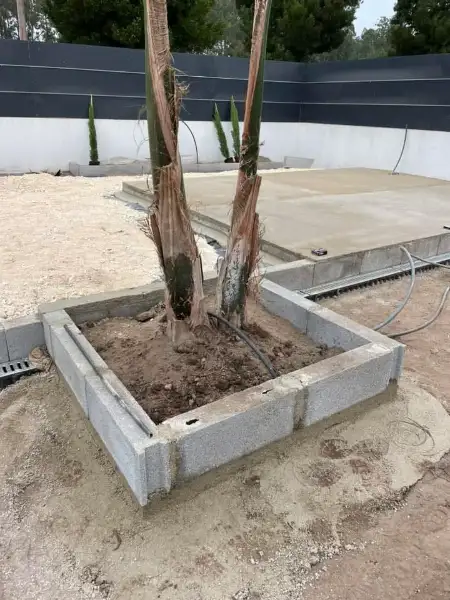 Jardim amplo com relva sintética, caminhos em lajes e zona de fogueira — durante a obra