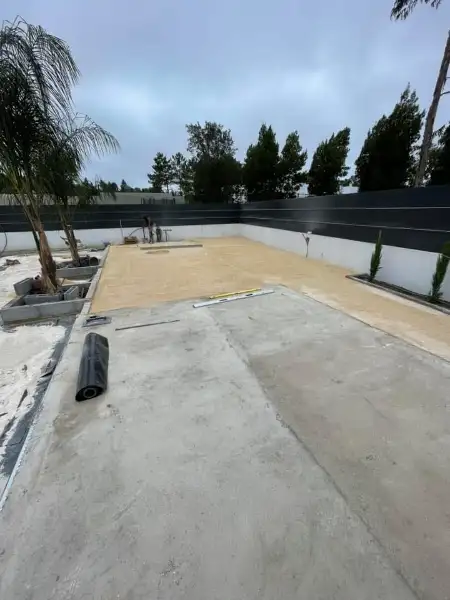 Jardim amplo com relva sintética, caminhos em lajes e zona de fogueira — durante a obra
