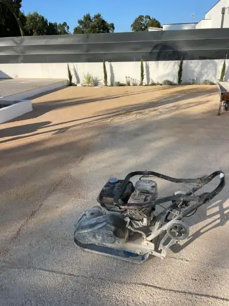 Jardim amplo com relva sintética, caminhos em lajes e zona de fogueira — durante a obra