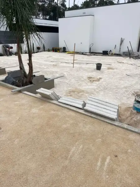Jardim amplo com relva sintética, caminhos em lajes e zona de fogueira — durante a obra