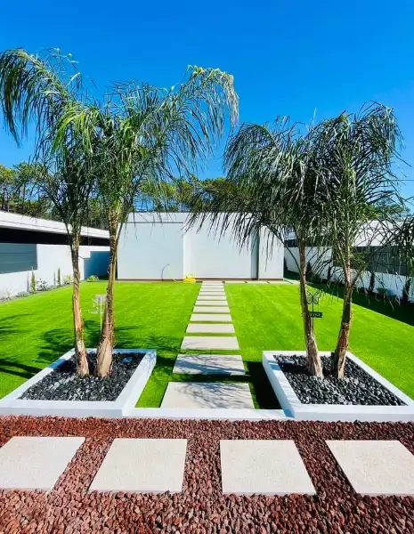 Jardim amplo com relva sintética, caminhos em lajes e zona de fogueira — resultado final