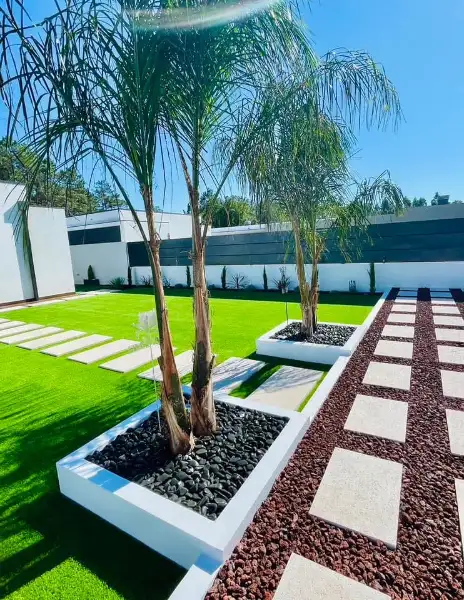 Jardim amplo com relva sintética, caminhos em lajes e zona de fogueira — resultado final