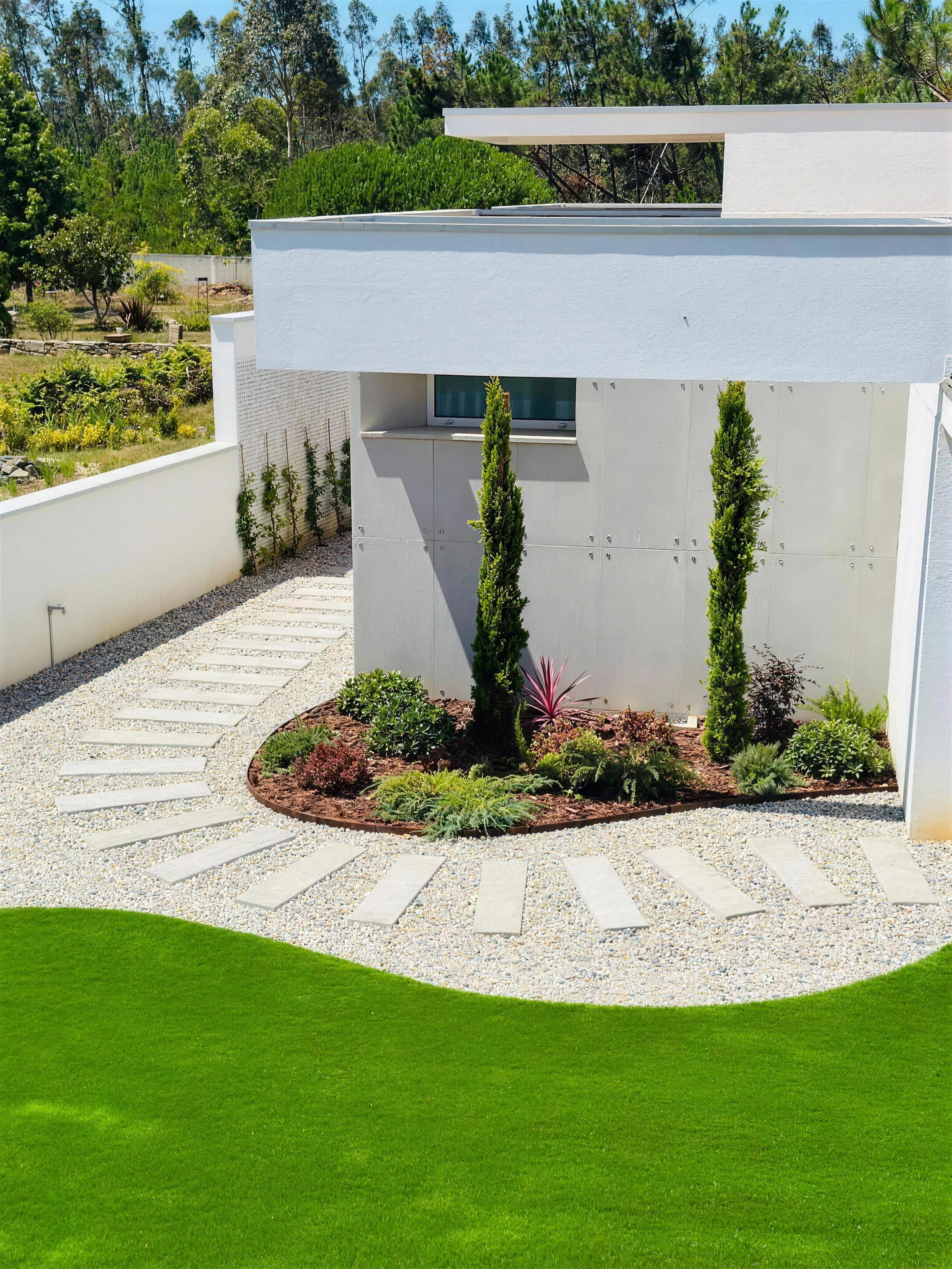 Jardim de moradia moderna com relva sintética, caminho de lajes em leque sobre seixo branco e canteiro com ciprestes