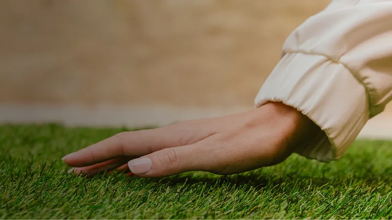 Mão a passar sobre as fibras de relva sintética Turfgrass